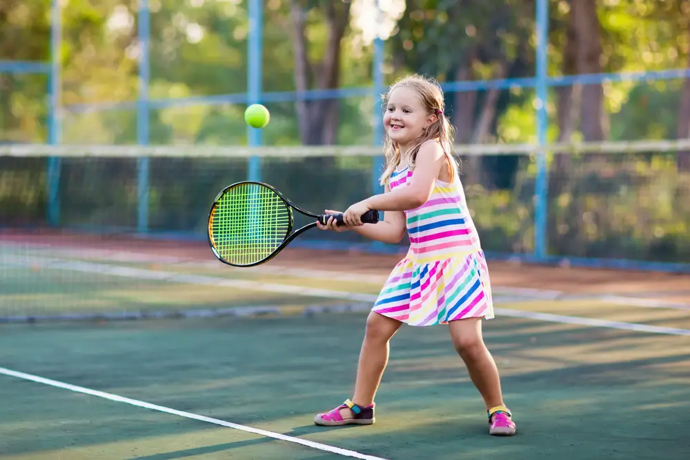 Child playing tennis on outdoor court.