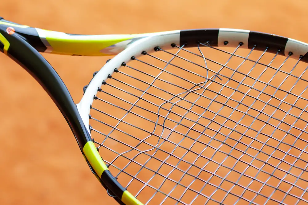 Tennis racket with broken strings close up.
