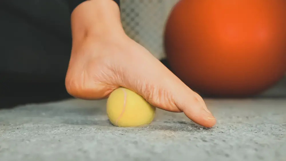Woman massaging her foot with tennis ball.