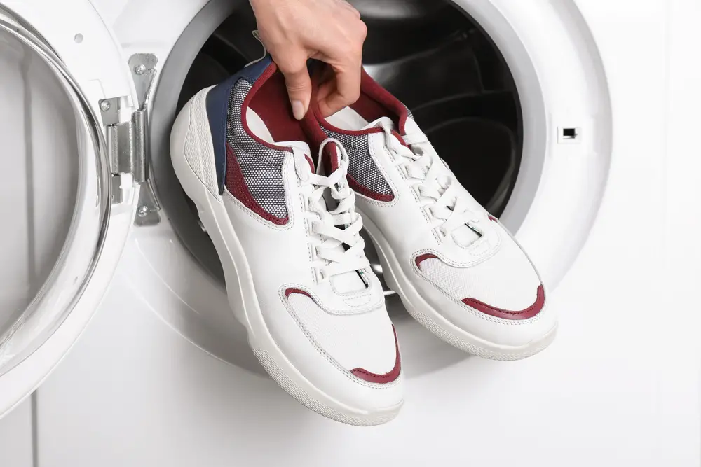 Woman putting pair of sport shoes into washing machine