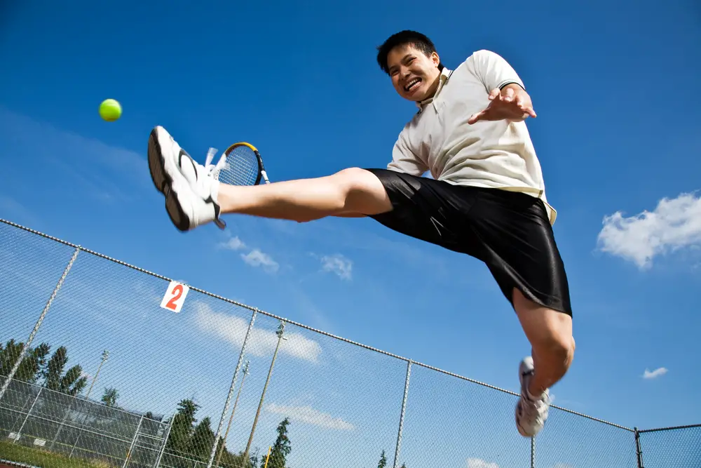 tennis player jumping in the air hitting a tennis ball