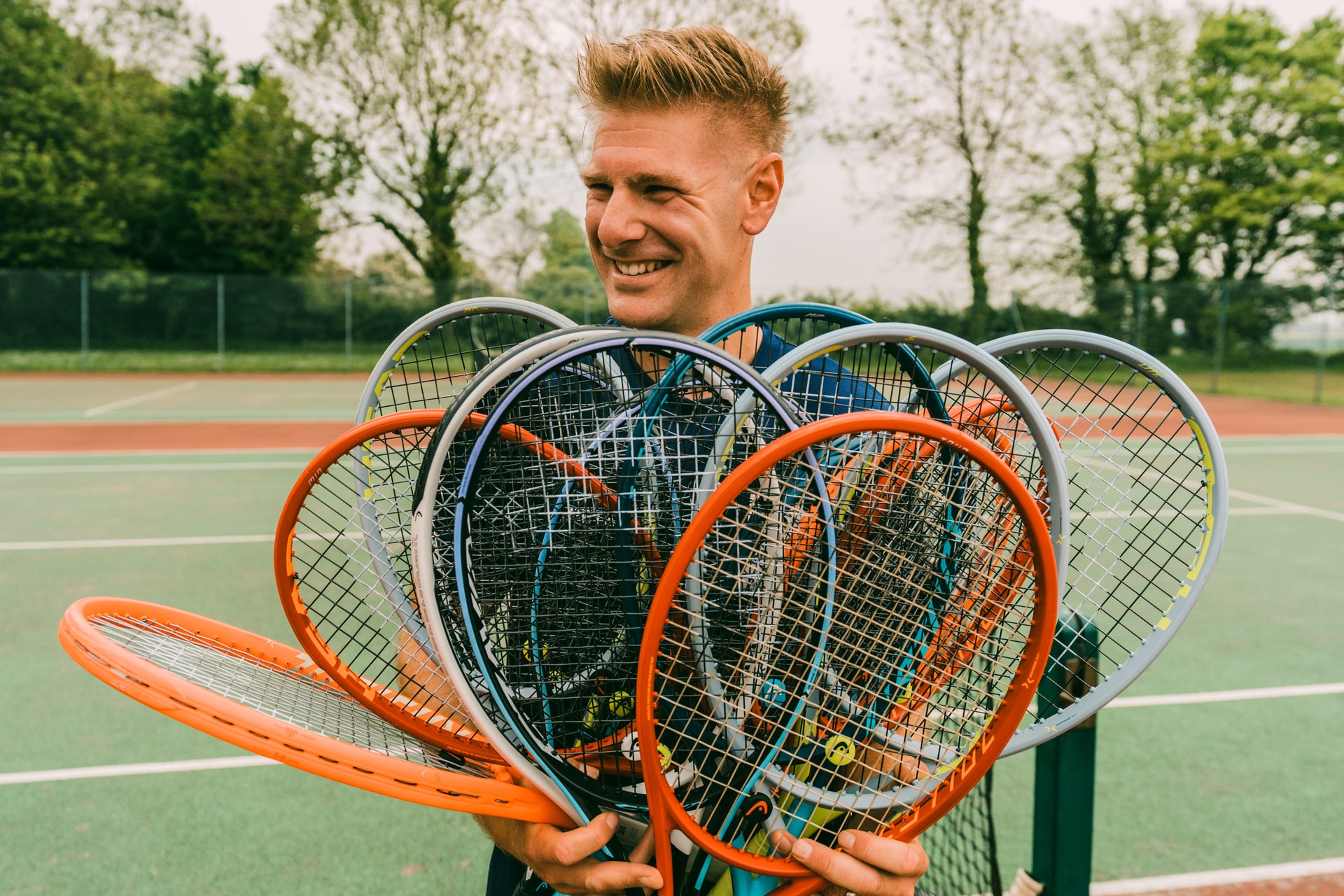 A man holding a bunch of different tennis rackets in his hands whilst smiling