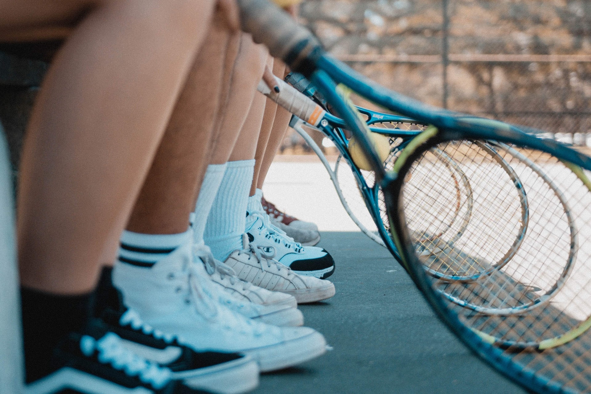 Five sets of legs sitting in a line with their tennis rackets touching the ground